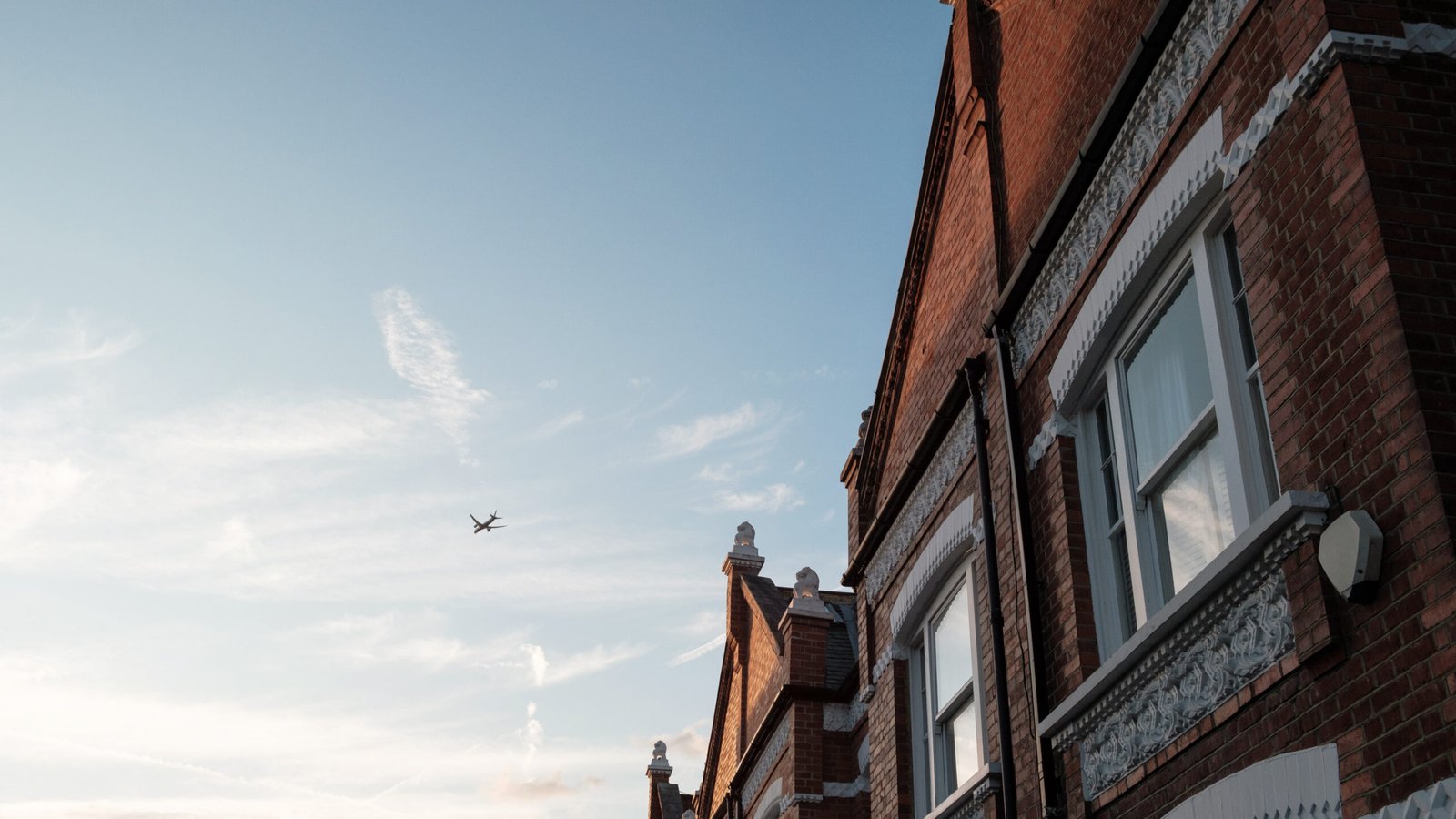 Airplane is flying in the sky over a row of typical english brick terraced houses in a london suburb at sunset